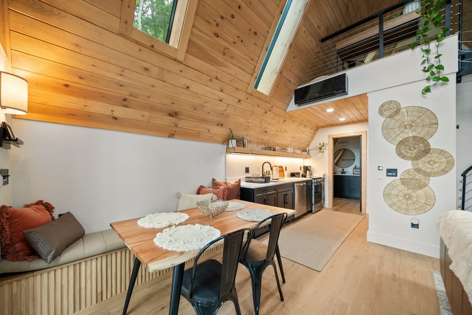 Built-in banquette, butcher-block dining table, and a bright kitchen all tucked under a soaring cedar ceiling with loft views above.