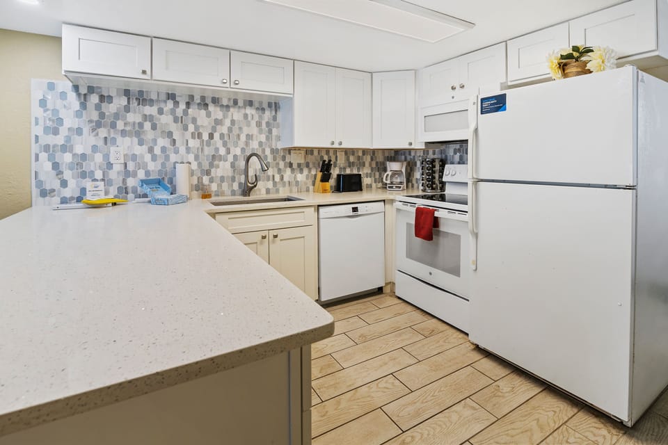 Bright and modern beachside kitchen featuring quartz countertops, full-size appliances, and ample space—perfect for preparing meals to enjoy during your oceanfront getaway.