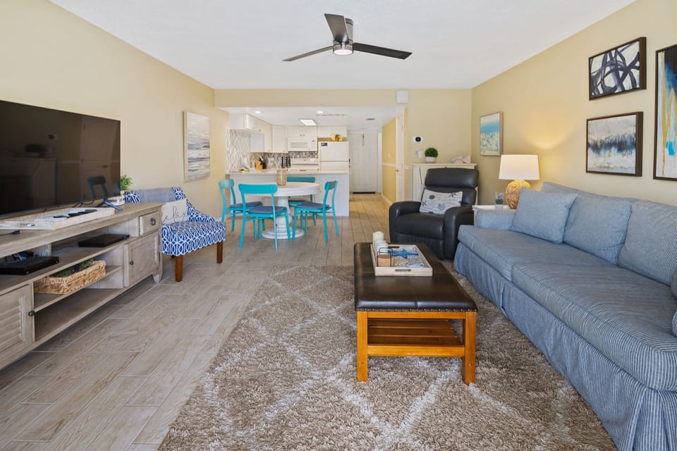Enjoy a spacious beachside condo with a comfortable living area, vibrant dining set, and open kitchen—perfect for relaxing after a day of oceanfront fun.
