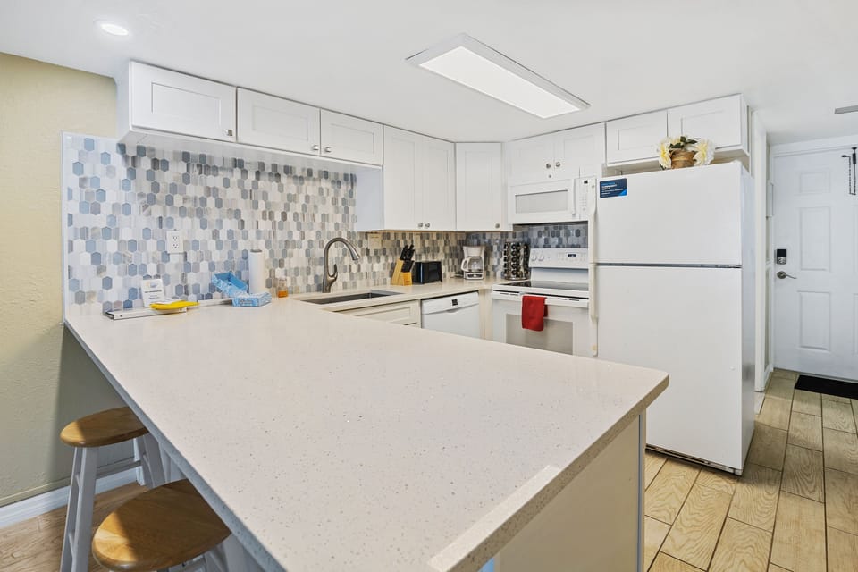 Fully equipped beachside kitchen with sleek white cabinetry, quartz countertops, and a stylish backsplash—perfect for preparing meals during your relaxing ocean getaway.