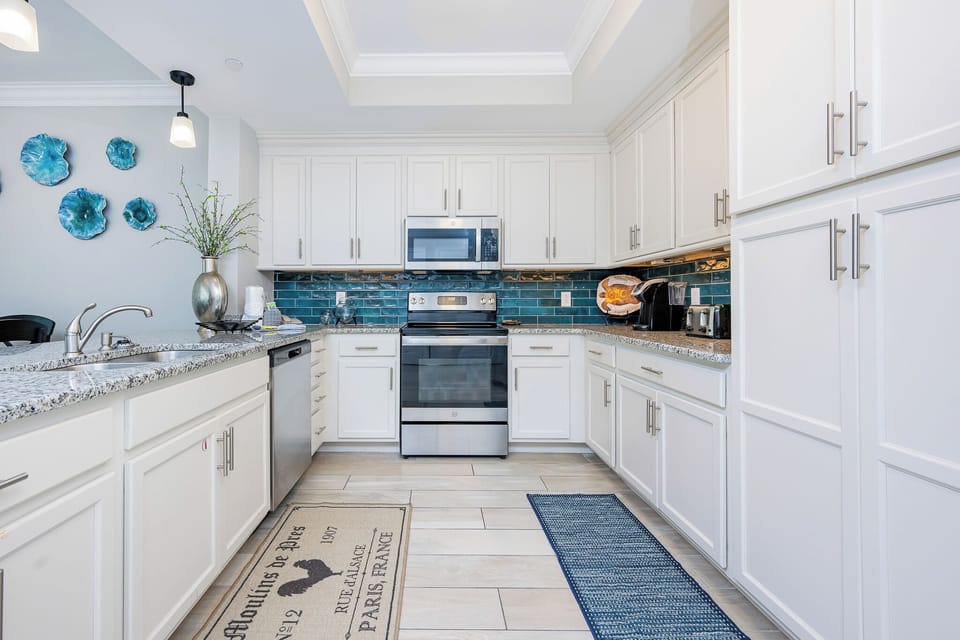 Prepare meals in this stylish kitchen with sleek cabinetry, stainless appliances, and teal backsplash