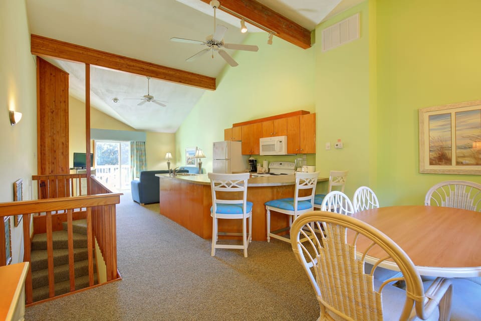 Open-concept kitchen and dining area with vaulted ceilings, natural wood accents, and a bright coastal palette ideal for relaxed beachside living.