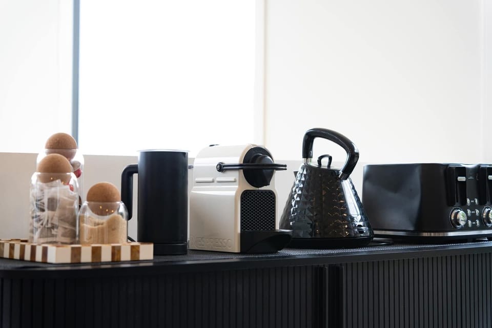 Everything you need for a morning pick-me-up—Nespresso machine, tea, kettle, and toaster—all set up on a sleek black sideboard.