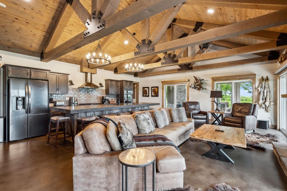 Sprawling lodge-style living room with soaring timber beams, rustic finishes, and an open layout that flows seamlessly into the gourmet kitchen—perfect for gathering after a day on the trails.