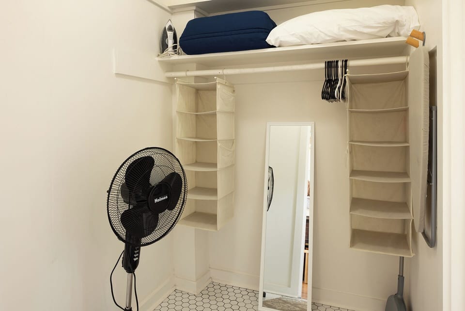 Closet with extra linens, fan, hangers and mirror
