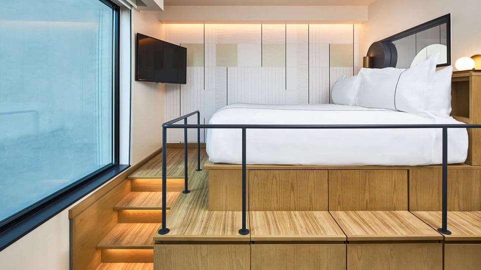 Steps lead to lofted bed next to large window and mounted TV