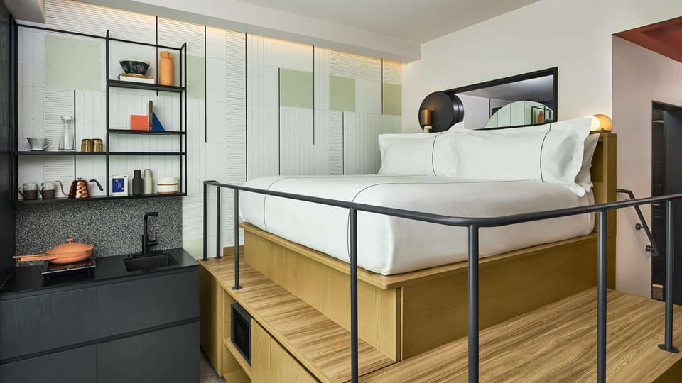 Lofted bed with rails next to small kitchen and open shelving