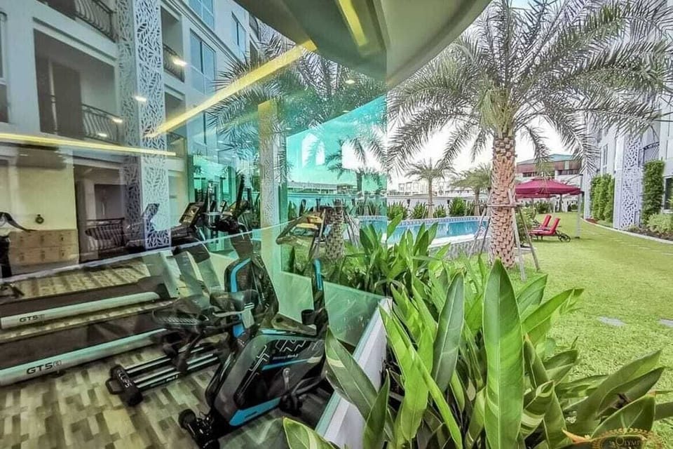 Depuis la salle : vue panoramique sur un jardin verdoyant et une piscine étincelante. Combinez exercice et détente dans un environnement naturel et luxueux. Palmiers, transats et verdure complètent ce cadre exceptionnel pour un séjour revitalisant
