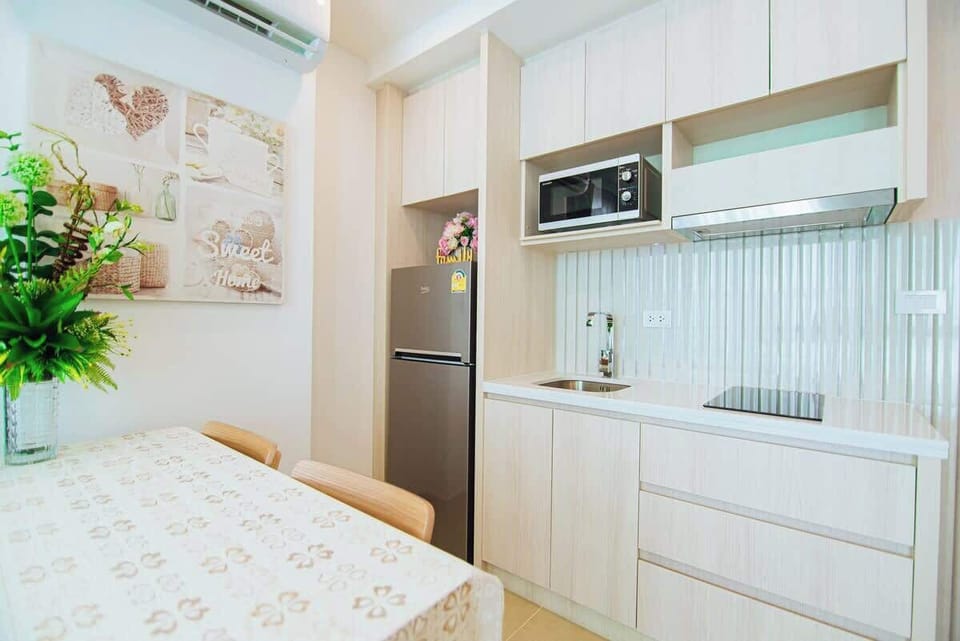 Cuisine moderne entièrement équipée avec micro-ondes, plaques de cuisson et réfrigérateur. Décoration chaleureuse avec tableau 'Sweet Home'. Parfaite pour préparer vos repas dans une ambiance cosy et conviviale.