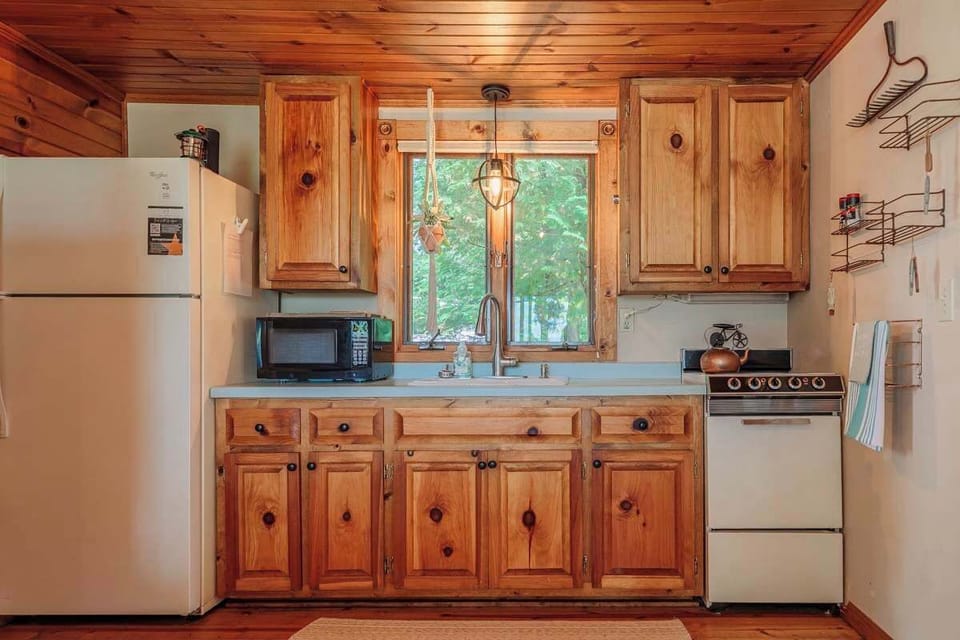 Kitchen view showcasing the refrigerator topped with a wireless speaker and lantern, alongside a small stove and microwave—everything you need for convenient meal prep in your charming waterfront cottage.