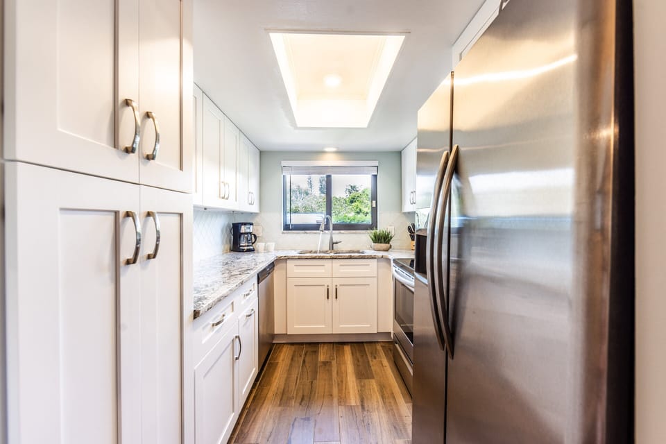 This bright, fully equipped kitchen features sleek stainless steel appliances, granite countertops, and a beach-inspired design—perfect for preparing meals during your relaxing seaside getaway.