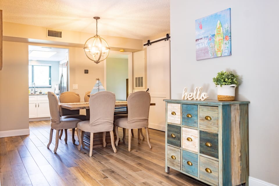 Gather for meals in this inviting beach-style dining area featuring a rustic coastal cabinet, elegant lighting, and warm wood tones—perfect for enjoying seaside living with friends and family.