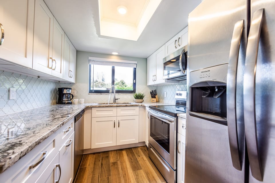 Whip up beach day meals in this full kitchen featuring stainless steel appliances, granite countertops, and a sunny window view. Perfect for family-friendly stays and seaside cooking convenience.