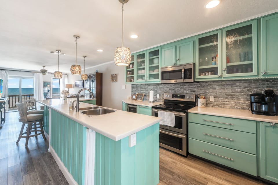 Your fully equipped kitchen features sea-green cabinets and ocean views, perfect for cooking meals while watching waves roll in.