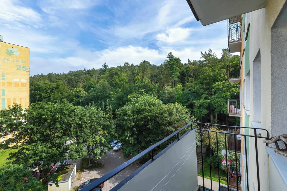 A balcony with metal railings overlooking a peaceful, green landscape and neighboring buildings.