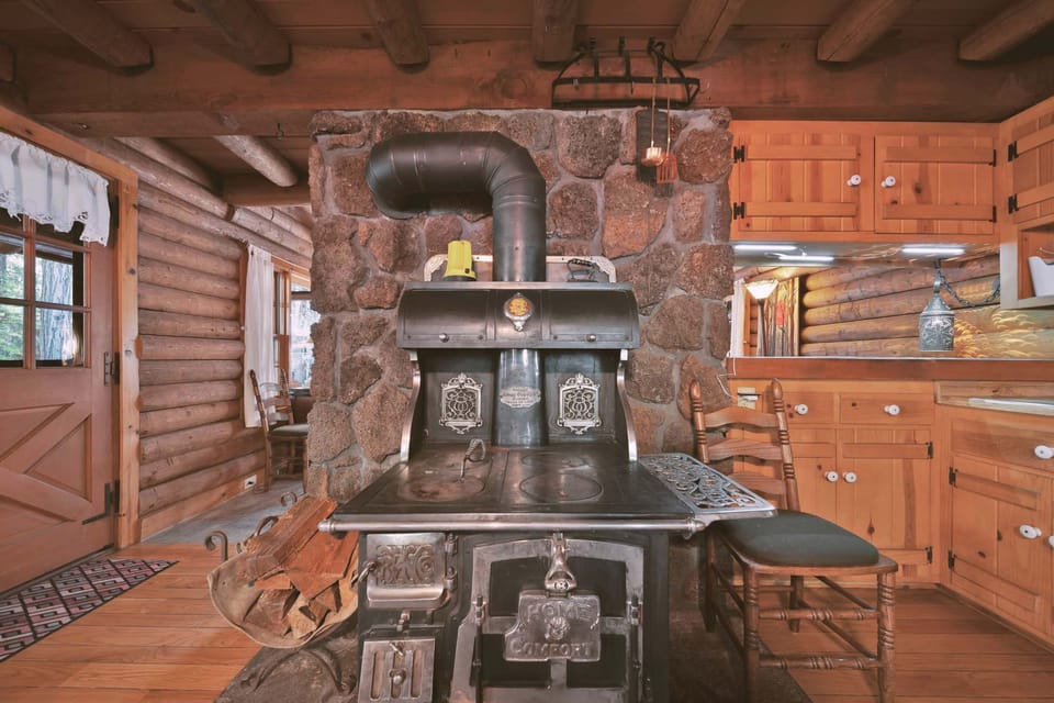 A standout feature of this area is the vintage cast iron wood-burning stove, set against a rustic stone backdrop—adding nostalgic charm.
