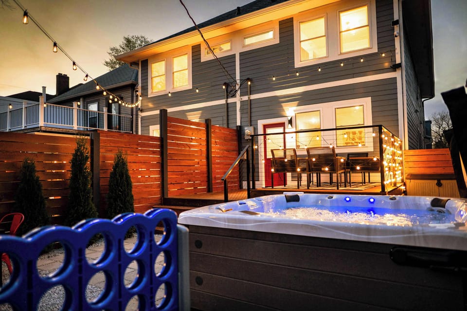 Relax in a serene backyard oasis with a bubbling hot tub, warm string lights, and cozy wood fencing. The glowing lights, rich wood, and cool blue tones create a peaceful, inviting atmosphere perfect for unwinding under the stars.