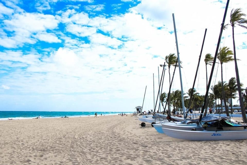 Stroll sandy shores beside sailboats and sparkling turquoise water.