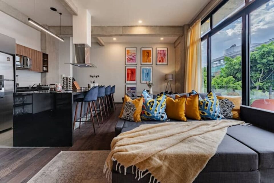 Open-plan living area with a comfortable sofa, throw blanket, and colorful artwork.