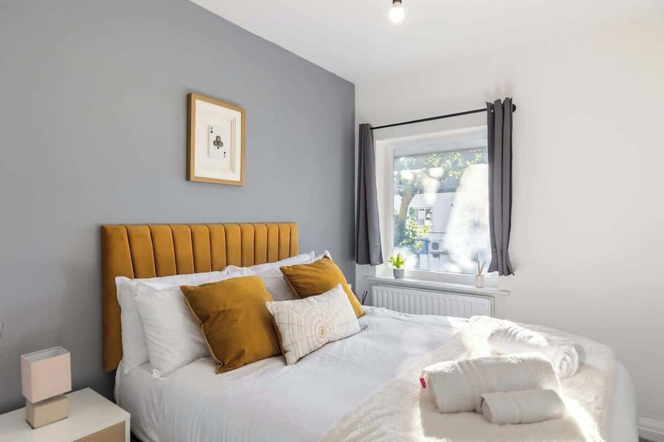 - Cozy bedroom with mustard accents and soft bedding  
- Grey feature wall adds modern style to your stay  
- Window view brings fresh light and calming vibes  
