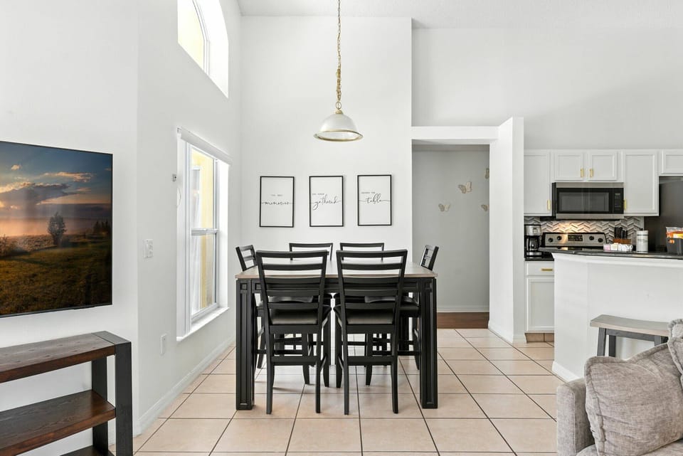 This bright dining area boasts a sleek black table with matching chairs, warm tile flooring, and striking wall art, all bathed in natural light to create an inviting space perfect for enjoying meals together.