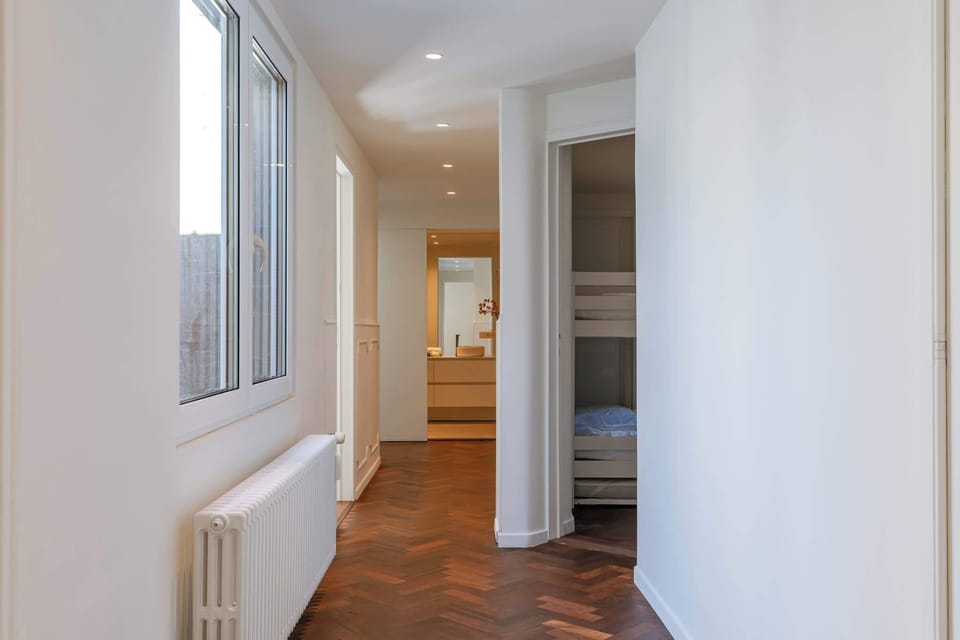 Bright hallway with wooden floors, large windows, and access to bedrooms and bathroom