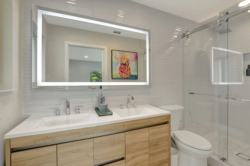 Refresh in a polished bathroom with a double vanity, backlit mirror, glass shower, and clean modern finishes.