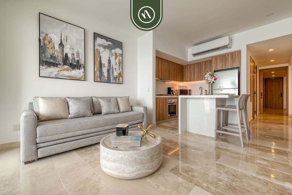 Bright open-plan great room layout combining a comfortable beige sofa, marble coffee table, and white kitchen breakfast bar.