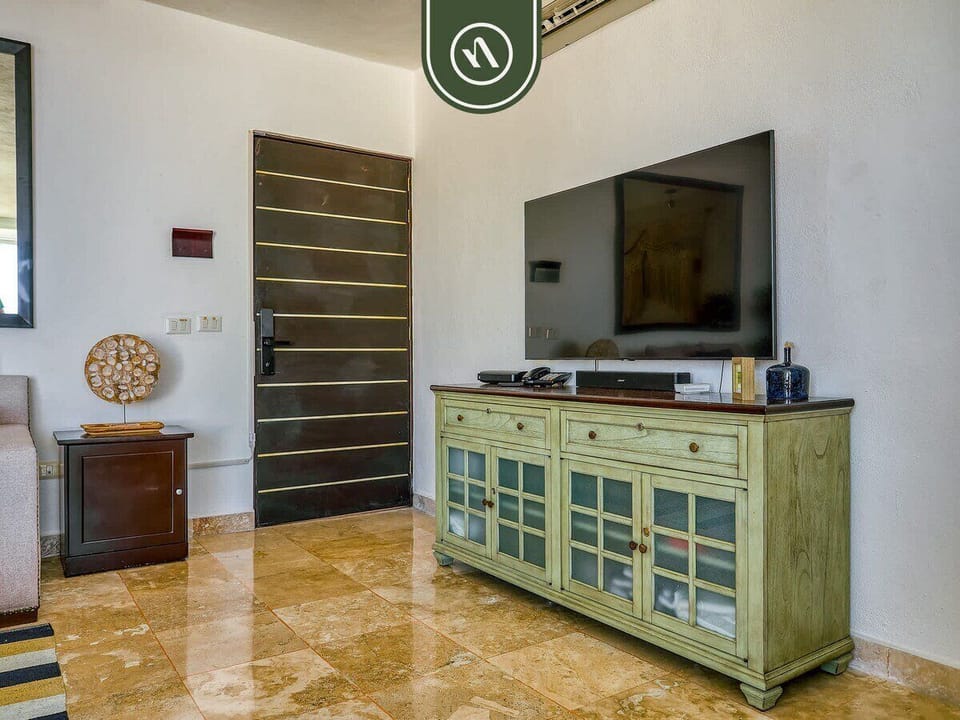 Spacious room view highlighting a rustic green media console table with a large flat-screen TV next to the main entrance door.