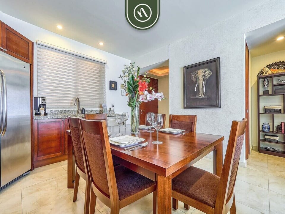 Enjoy home-cooked meals in this inviting dining area. It features a sturdy wooden table with matching chairs, tasteful artwork, and an open layout connecting seamlessly to the kitchen.
