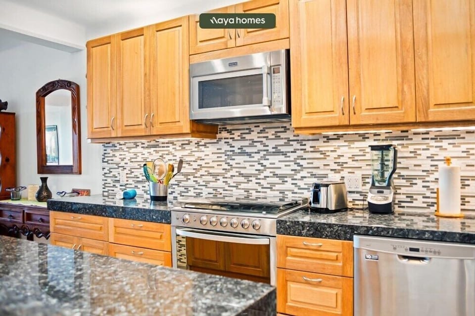 Home kitchen corner detailing a dark granite countertop, mosaic tile backsplash, and stainless steel appliances.