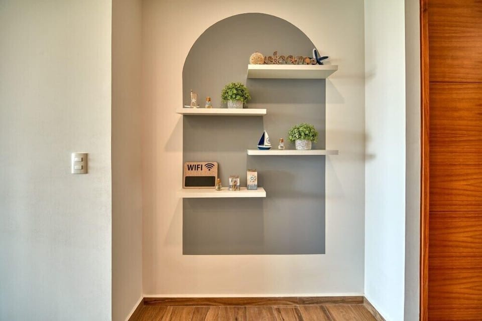 Elegant arched wall painted in grey, featuring white floating shelves arranged with small plants and coastal ornaments.