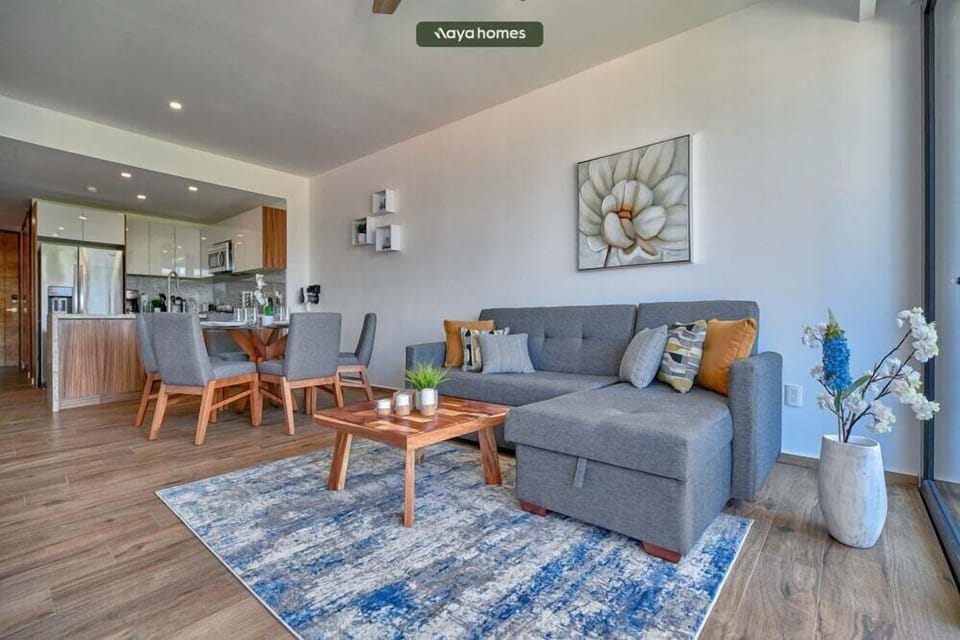 Welcoming lounge space featuring a grey sectional sofa, an artistic blue and white area rug, a wooden coffee table, and the dining area in the background.