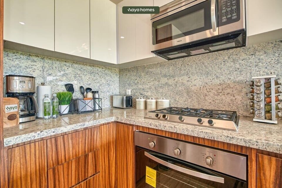 Detailed view of a modern built-in stovetop, stainless steel oven, and overhead microwave surrounded by a speckled granite backsplash.