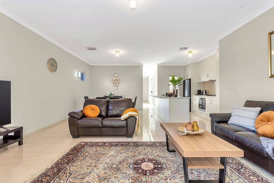 Unwind in the welcoming living area with leather sofas, a large TV, and direct flow to dining and kitchen—designed for effortless relaxation.