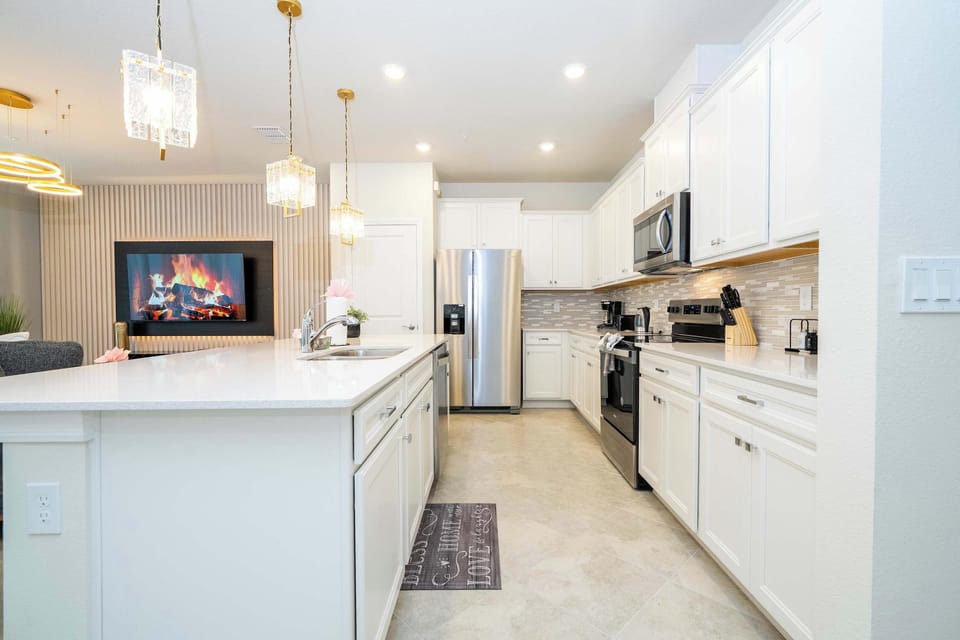 Cook and entertain in this stunning kitchen featuring stainless steel appliances, elegant pendant lighting, and a cozy fireplace view from the island.