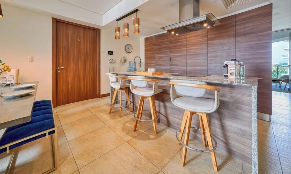 Bright open-concept perspective showing three sleek white bar stools lined up along the warm wood-paneled breakfast island.