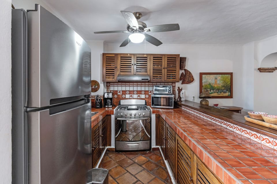 A rustic-style kitchen equipped with modern stainless steel appliances, louvered wooden cabinets, and distinctive terracotta tile countertops.
