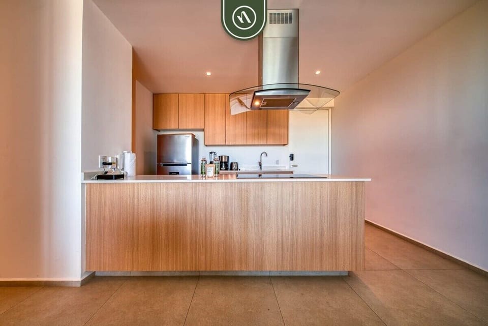 This bright, minimalist kitchen boasts warm wood-toned cabinetry, a sleek breakfast bar, and high-end stainless steel appliances. The open layout is perfect for entertaining while you cook.