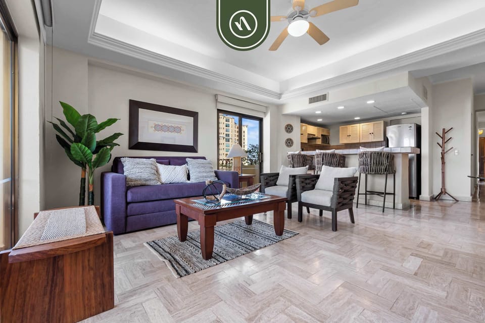 Comfortable lounge space showcasing a purple sofa, a wooden coffee table, patterned tile flooring, and a kitchen breakfast counter in the background.