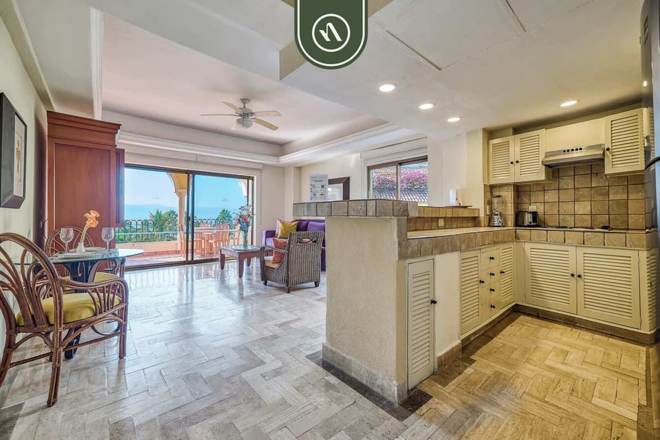 Spacious room layout showcasing a rustic tiled breakfast bar counter, white kitchen cabinetry, and polished pattern-tiled floors leading toward the living lounge.