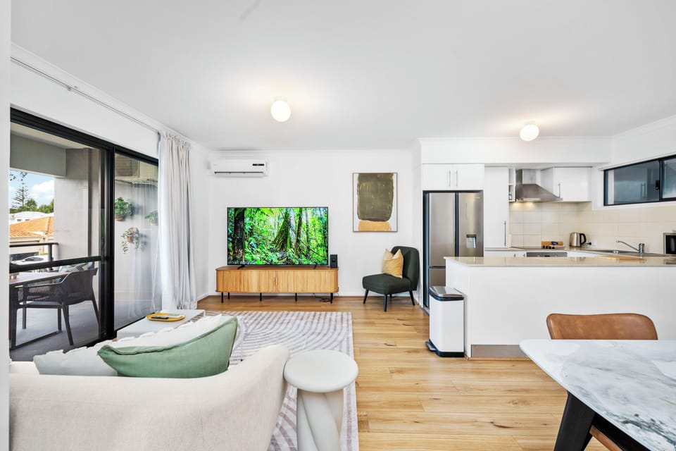 Bright and spacious open-plan living with a large smart TV, balcony access, and a fully equipped kitchen for easy entertaining.
