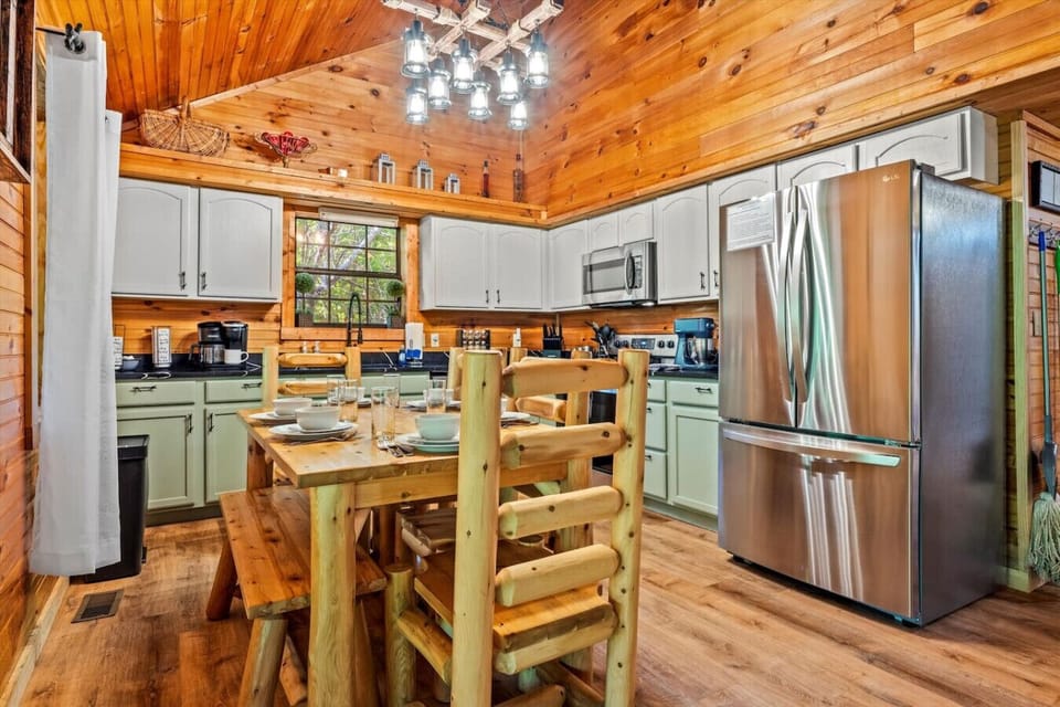The open kitchen and dining area includes natural log furniture, modern appliances, and a warm glow from the cabin’s wood interior. Whether it’s a pancake breakfast or a late-night snack, this space makes every meal feel special.