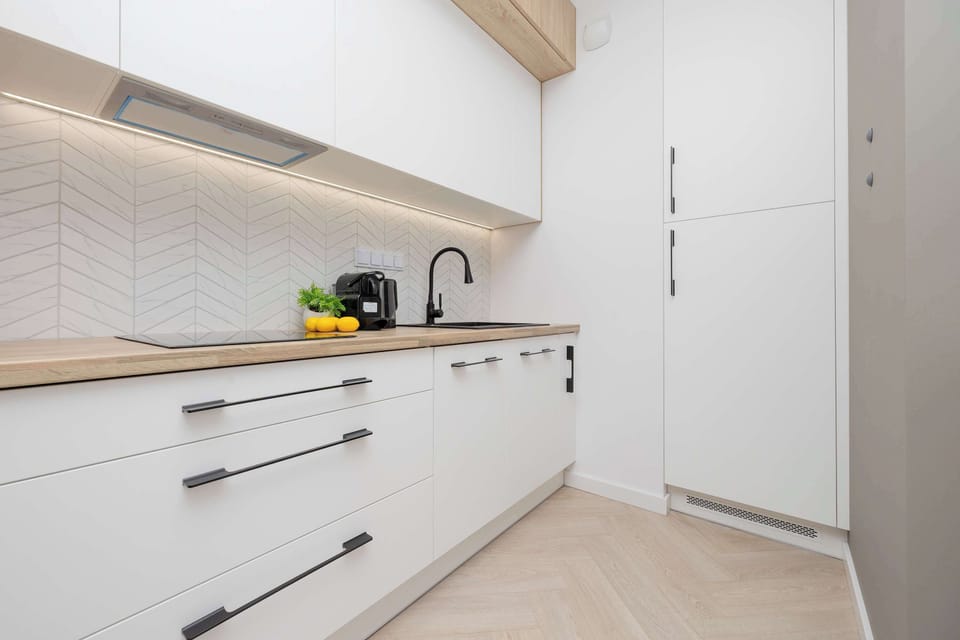 A sleek white kitchen with built-in appliances and minimalist design. Wooden accents add warmth to the clean, contemporary aesthetic.