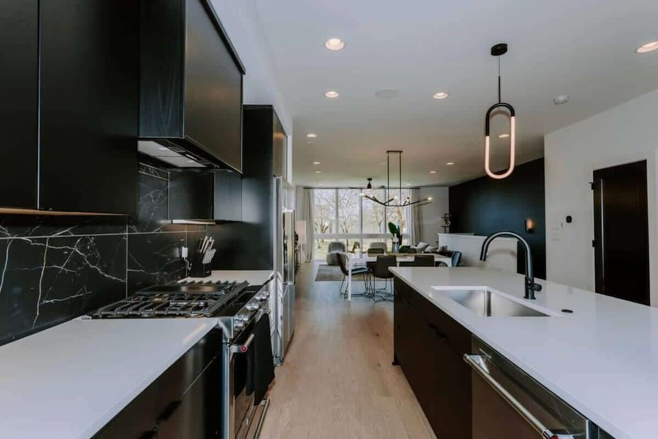 A modern, sleek kitchen interior with black cabinets, stainless steel appliances, and a marble-like backsplash