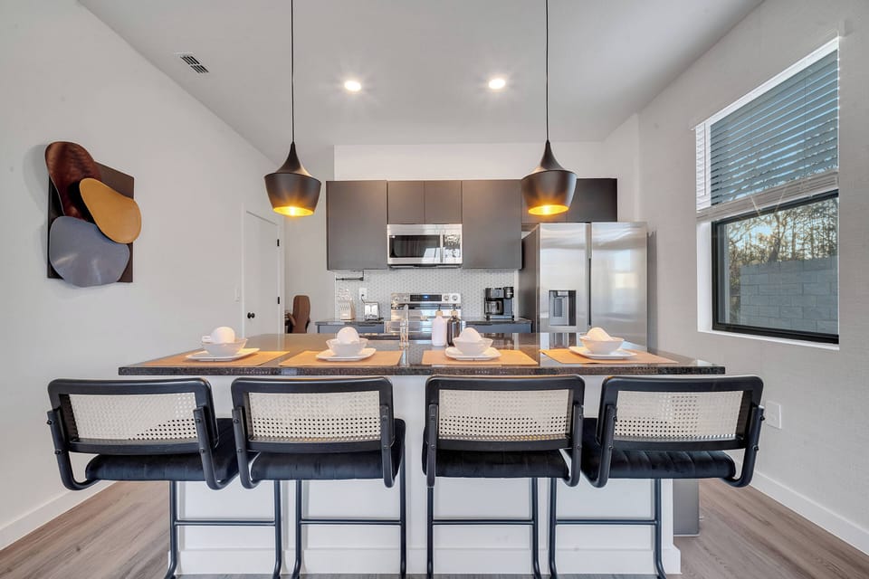 Experience culinary delights in this stylish kitchen, featuring sleek dark cabinetry and modern appliances. The warm glow from pendant lights above the spacious island creates an inviting atmosphere, perfect for gathering.