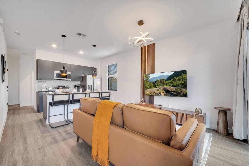 Experience a bright contemporary living area featuring a cozy leather sofa adorned with a stylish throw. The sleek kitchen, with its trendy pendant lighting, is perfect for your culinary adventures just a few steps away.