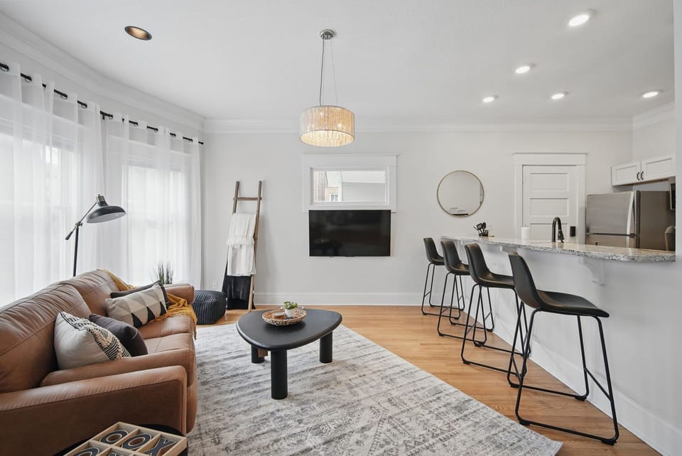Bright and inviting living space featuring a modern leather sofa, wall-mounted smart TV, and playful textures—ideal for relaxing after a day out.