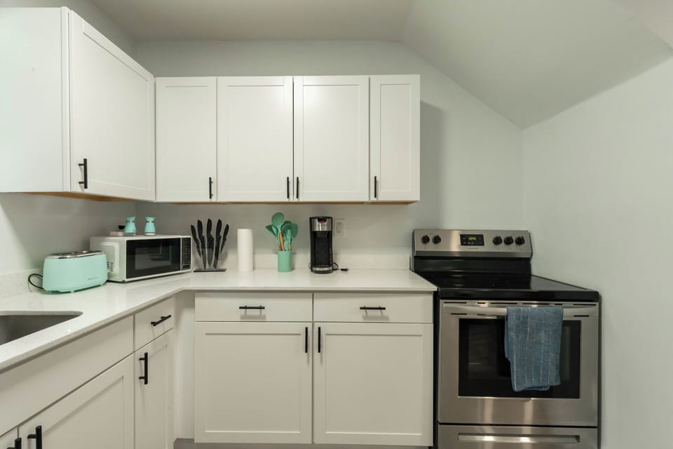 Bright kitchen with stainless steel oven, microwave, and full cookware set.