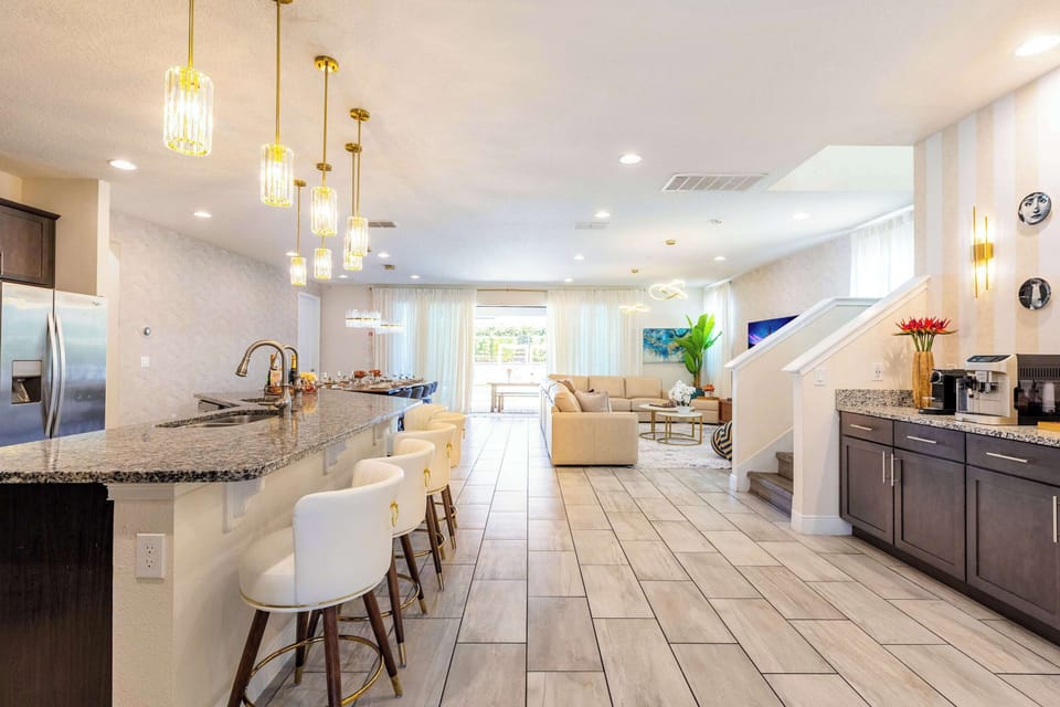 The open floor plan in full view — chef's kitchen, great room, and sitting area flowing into one continuous space, with the second-floor landing above. The scale that lets eleven bedrooms feel like one home.
